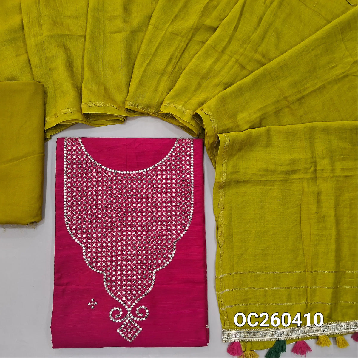 Dark pink semi raw silk unstitched salwar material, sequins work on yoke,(lining needed)mehandhi green spun cotton bottom, silk cotton dupatta with colorful tassels and fancy lace tapping. OC260410