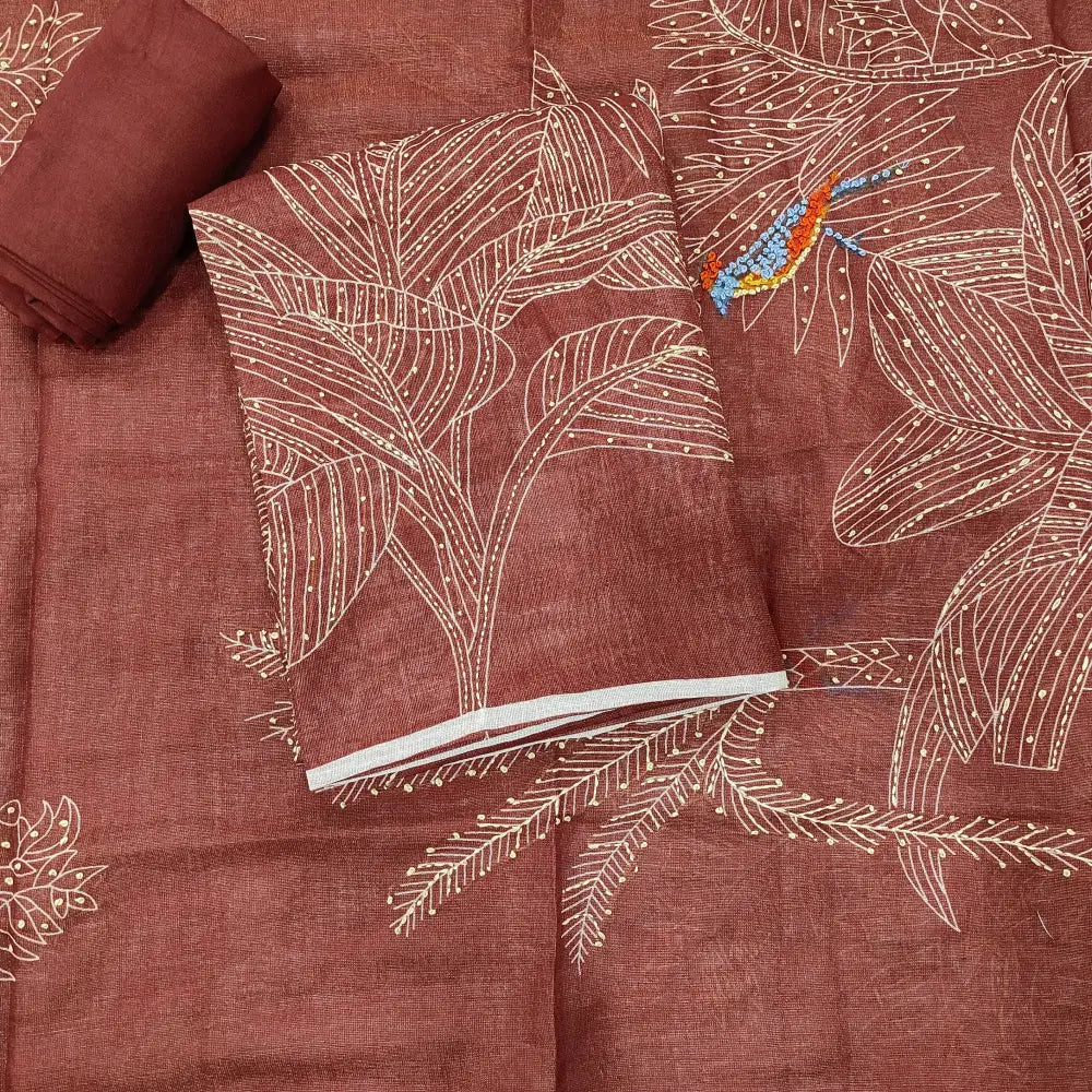 Rust-colored fabric with white embroidered palm leaf patterns and a small blue bird detail